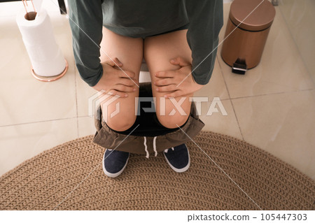 Boy suffering from hemorrhoid on toilet bowl in rest room, closeup 105447303