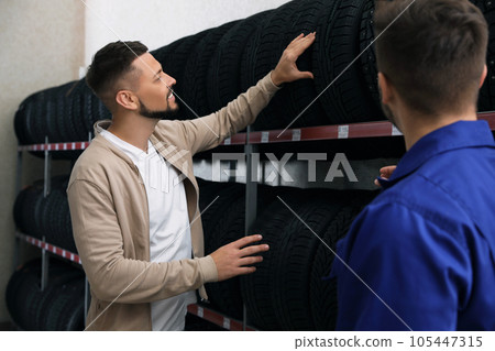 Mechanic helping client to choose car tire in auto store 105447315