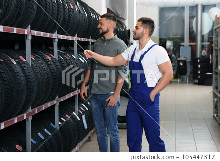 Mechanic helping client to choose car tire in auto store 105447317