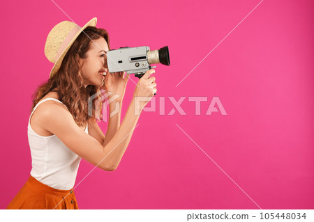 Beautiful young woman using vintage video camera on crimson background, space for text Beautiful young woman using vintage video camera on crimson background, space for text 105448034