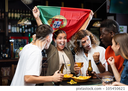 Happy international sport fans waving the flag of Portugal while drinking beer and watching tournament in sport bar Happy international sport fans waving the flag of Portugal while drinking beer and watching tournament in sport bar 105450621