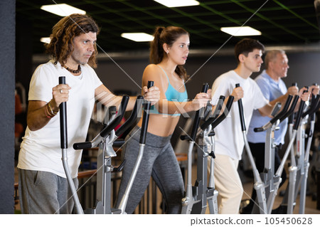Concentrated man working out on elliptical machine in gym Concentrated man working out on elliptical machine in gym 105450628