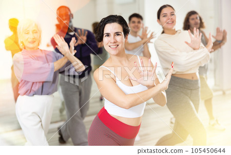 Smiling young woman rehearsing modern dance with group in dance school 105450644