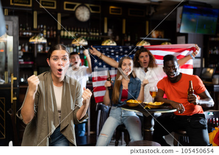 Multiracial soccer supporters waving flag of USA while resting with beer and chips in the sport bar Multiracial soccer supporters waving flag of USA while resting with beer and chips in the sport bar 105450654