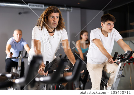 Man and woman taking indoor cycling class at fitness center, doing cardio riding bike 105450711