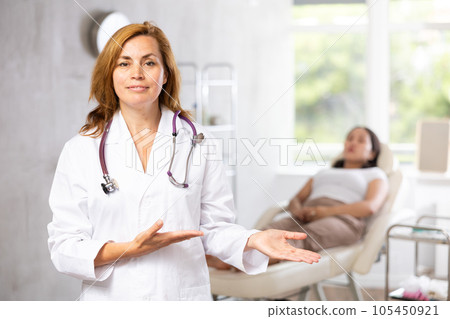 Portrait of female doctor cosmetologist wearing white overall showing equipment of clinic before procedure Portrait of female doctor cosmetologist wearing white overall showing equipment of clinic before procedure 105450921