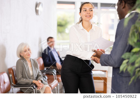 Woman makes deal, shaking hands with middle-aged African man colleague while standing in office 105450922