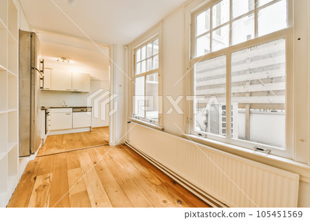 an empty living room with wood flooring and white walls in the room is very large, bright window view 105451569