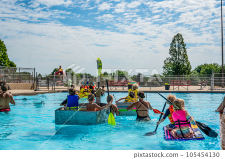 Two small kids paddling a cardboard boat in a race in a pool Two small kids paddling a cardboard boat in a race in a pool 105454130