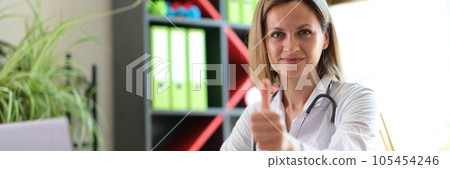 Female doctor sitting at her desk in medical clinic and shows thumb up. Female doctor sitting at her desk in medical clinic and shows thumb up. 105454246