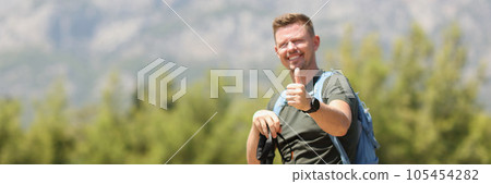 Happy hiker with backpack showing thumbs up against background of mountains on sunny day. Happy hiker with backpack showing thumbs up against background of mountains on sunny day. 105454282