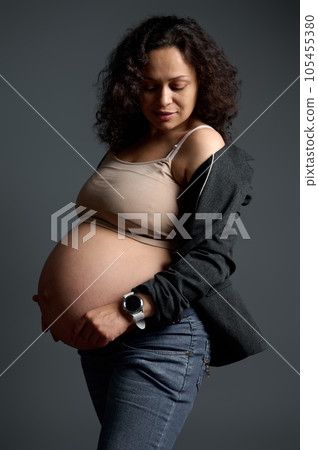 Curly haired Latin American pregnant woman, expectant mother touching her big belly in the ninth month of her pregnancy Curly haired Latin American pregnant woman, expectant mother touching her big belly in the ninth month of her pregnancy 105455380