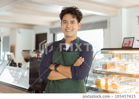 Young Asian male barista in apron having arms folded and smiling while looking at camera with copy space 105457415