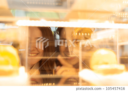 Asian smiling couple looking at cakes through the glass in the bakery and coffee shop. Man and woman pointing and ordering desserts while dating Asian smiling couple looking at cakes through the glass in the bakery and coffee shop. Man and woman pointing and ordering desserts while dating 105457416