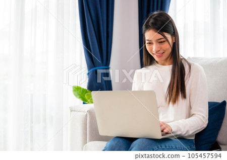 Young asian woman using laptop while seated on couch at home 105457594