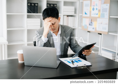 Frustrated young businessman working on a laptop computer sitting at his working place in office 105460889