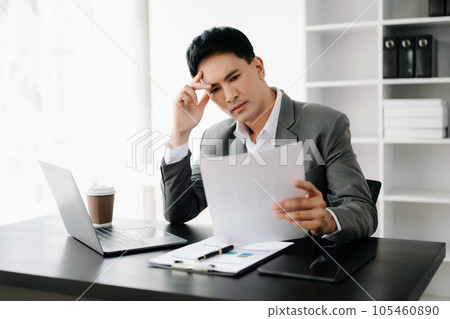 Frustrated young businessman working on a laptop computer sitting at his working place in office 105460890