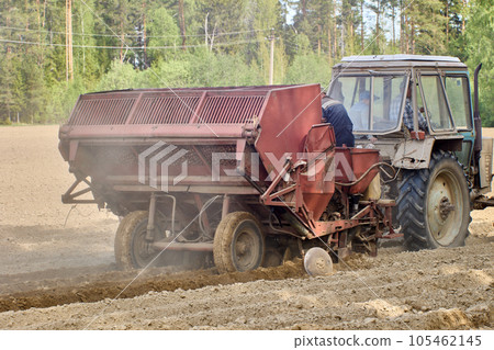 Potato planter is hitched to an agricultural wheeled tractor during spring sowing in plowed farmer field. 105462145
