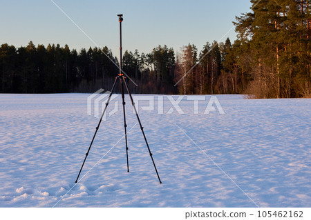 Tripod for photographer camera stands on snowy crust on winter evening. Tripod for photographer camera stands on snowy crust on winter evening. 105462162