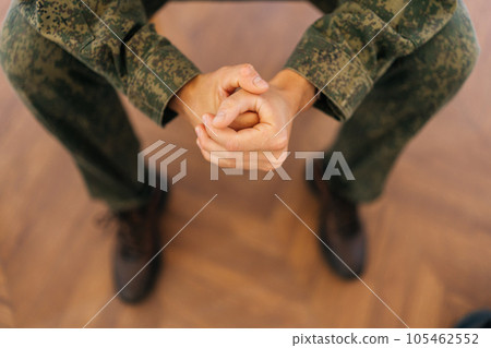 Close-up high-angle view of unrecognizable soldier male in camouflage uniform tightly clenching fists sitting in circle during PTSD group therapy session. Concept of mental health, psychotherapy 105462552