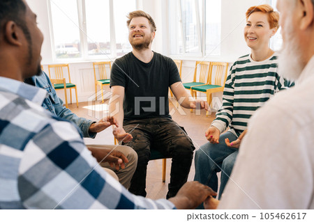 Group of happy multiracial people holding hands sitting in circle during therapy session. Cheerful multicultural and different ages men and women celebrating common progress and supporting each other. Group of happy multiracial people holding hands sitting in circle during therapy session. Cheerful multicultural and different ages men and women celebrating common progress and supporting each other. 105462617