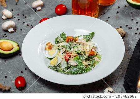 Traditional caesar salad in a white bowl on a old white table with leaves and a sauce boat and parmesan. Selected focus. 105462662