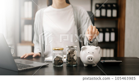 Woman holding coins putting in glass with using smartphone and calculator to calculate concept saving money for finance accounting. money coin into piggy bank 105463985