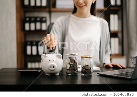 Woman holding coins putting in glass with using smartphone and calculator to calculate concept saving money for finance accounting. money coin into piggy bank 105463986