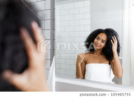 Smiling female looking at her reflection in a mirror and adjusting her hair	 105465755