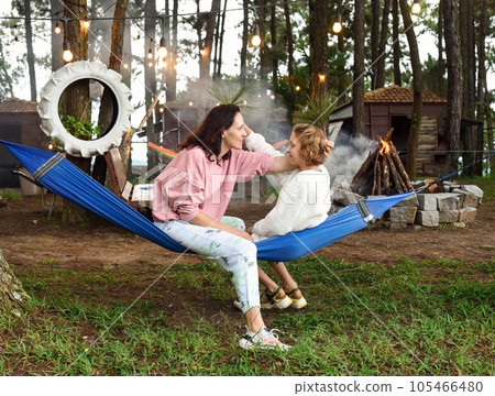 Mother and her daughter fooling around and sitting in hammock in the evening 105466480