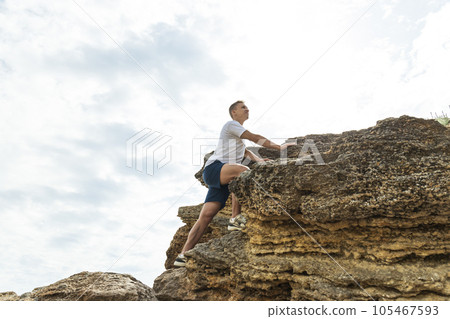 A man with an athletic build climbs to the top of a rock 105467593