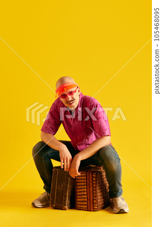Tired man in cap sitting on luggage against bright yellow background. Tired man in cap sitting on luggage against bright yellow background. 105468095