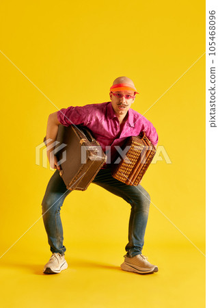 Photoshot of funky man in cap holding huge bags against bright yellow background. Photoshot of funky man in cap holding huge bags against bright yellow background. 105468096