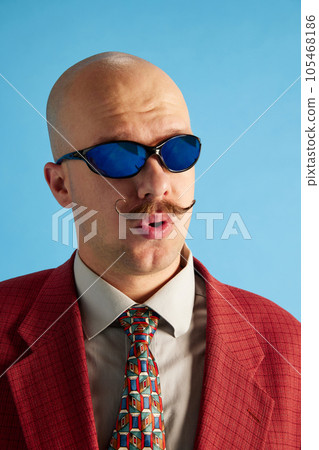 Headshot of whistles balded man with mustache dressed in business retro suit sneaking over blue studio background. 105468186