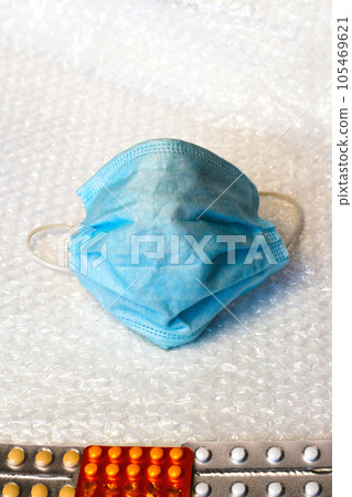 Defocus. The metaphor of a face in a blue medical mask looks at blisters of different pills. Virus and pandemic 105469621