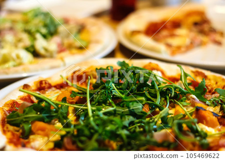 View Of Fresh Pizza With Arugula At Restaurant. tasty baked pizza decorated with green arugula and salmon in restaurant. Two plate with different pizzas on blur background. Selective focus 105469622