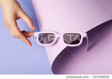 Sunglasses in hand on purple background, close up 105469698