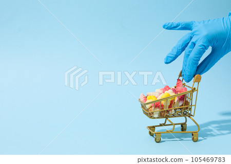 Jelly candies in shopping trolley and hand in medical glove on blue background, space for text 105469783