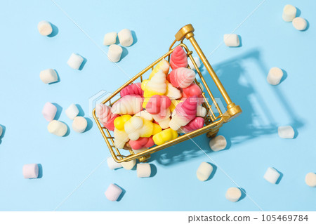 Jelly candies in shopping trolley and marshmallows on blue background, top view Jelly candies in shopping trolley and marshmallows on blue background, top view 105469784