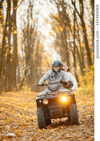 A young caucasian man and woman riding an ATV quad bike in autumn forest. Couple maneuvering off-road ATV. Couple wearing grey sportive costumes. A young caucasian man and woman riding an ATV quad bike in autumn forest. Couple maneuvering off-road ATV. Couple wearing grey sportive costumes. 105469869