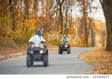 A young caucasian man and woman riding an ATV quad bikes in autumn forest. Couple maneuvering off-road ATV. Couple wearing grey sportive costumes. A young caucasian man and woman riding an ATV quad bikes in autumn forest. Couple maneuvering off-road ATV. Couple wearing grey sportive costumes. 105469877