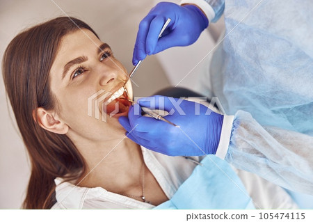 Professional doctor is doing tooth surgery to happy caucasian woman in modern dental cabinet 105474115