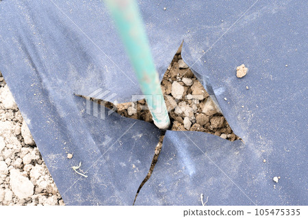A man drills a hole with a hand drill through agro fiber, field and manual work. 105475335