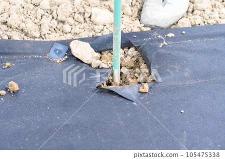A man drills a hole with a hand drill through agro fiber, field and manual work. 105475338
