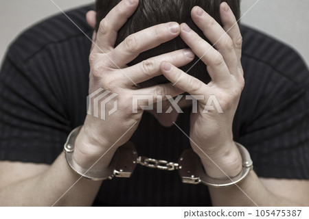 Handcuffed man covering his face with his hands. Handcuffed man covering his face with his hands. 105475387