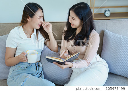 lgbtq, LGBT concept, homosexuality, portrait of two Asian women posing happy together and showing love for each other while having coffee at the dining table. lgbtq, LGBT concept, homosexuality, portrait of two Asian women posing happy together and showing love for each other while having coffee at the dining table. 105475499