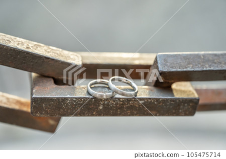 Two hands with wedding rings rest on a strong anchor chain 105475714