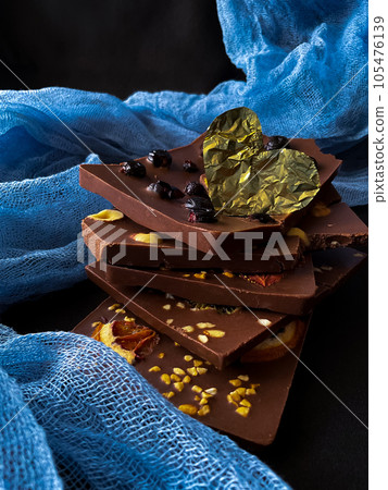 Pieces of chocolate with golden foil heart. With berries, strawberries, oranges 105476139