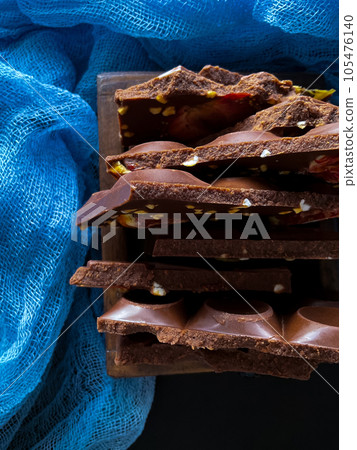 Pieces of chocolate with nuts and raisins on a dark background Pieces of chocolate with nuts and raisins on a dark background 105476140