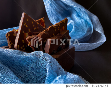 Pieces of chocolate with nuts and raisins on a dark background 105476141